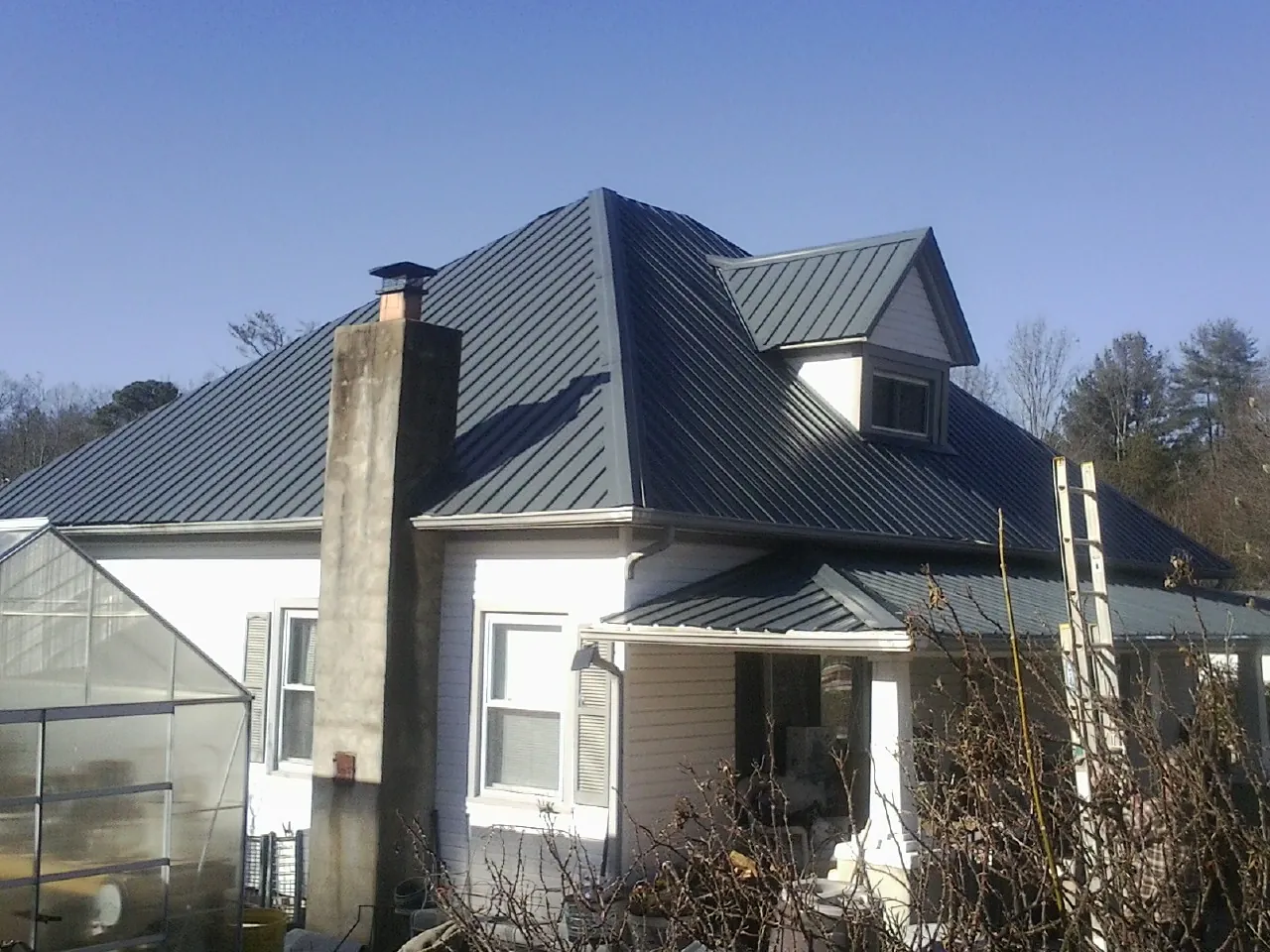Dark blue standing seam metal roof on a white farmhouse with dormer — Slate & Tile Roof Repair by Roofing Brothers in New Berlin