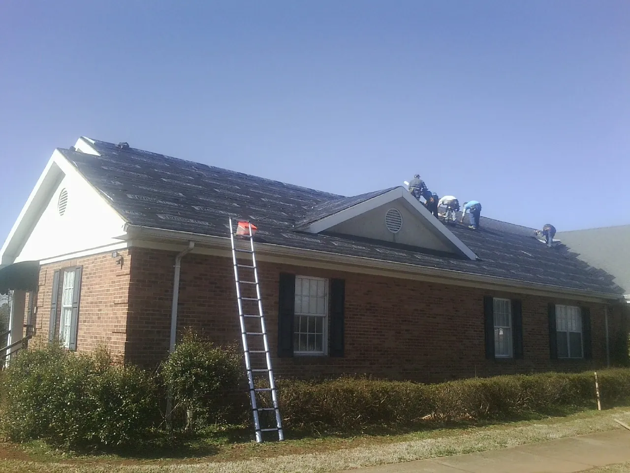 Crew tearing shingles off a brick ranch roof with a ladder set — Metal Roof Repair work by our crew in New Berlin